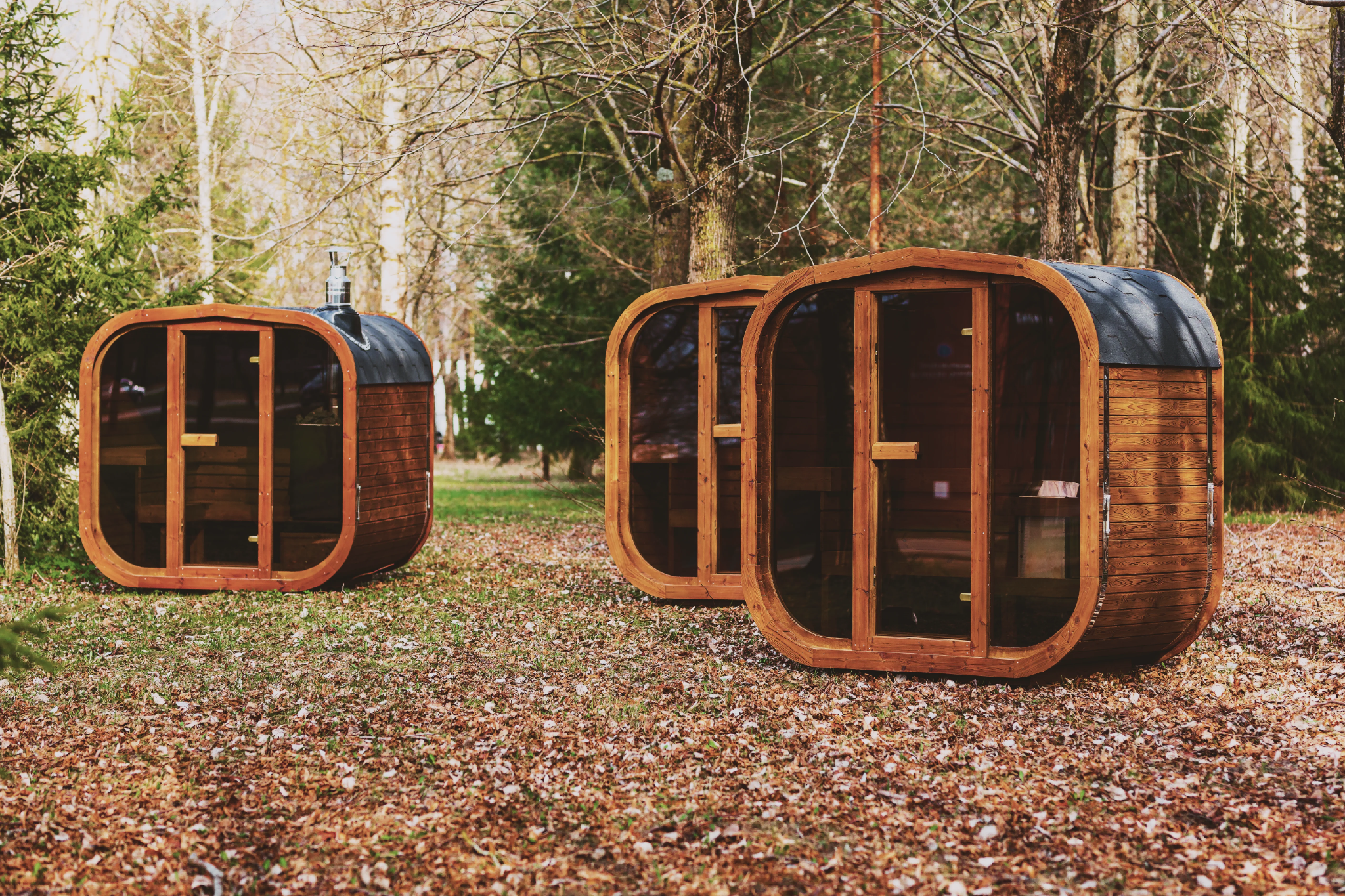 Mande Spa USA MW16 outdoor saunas made from sustainably sourced thermowood, featuring modern glass doors and set on a leafy forest floor